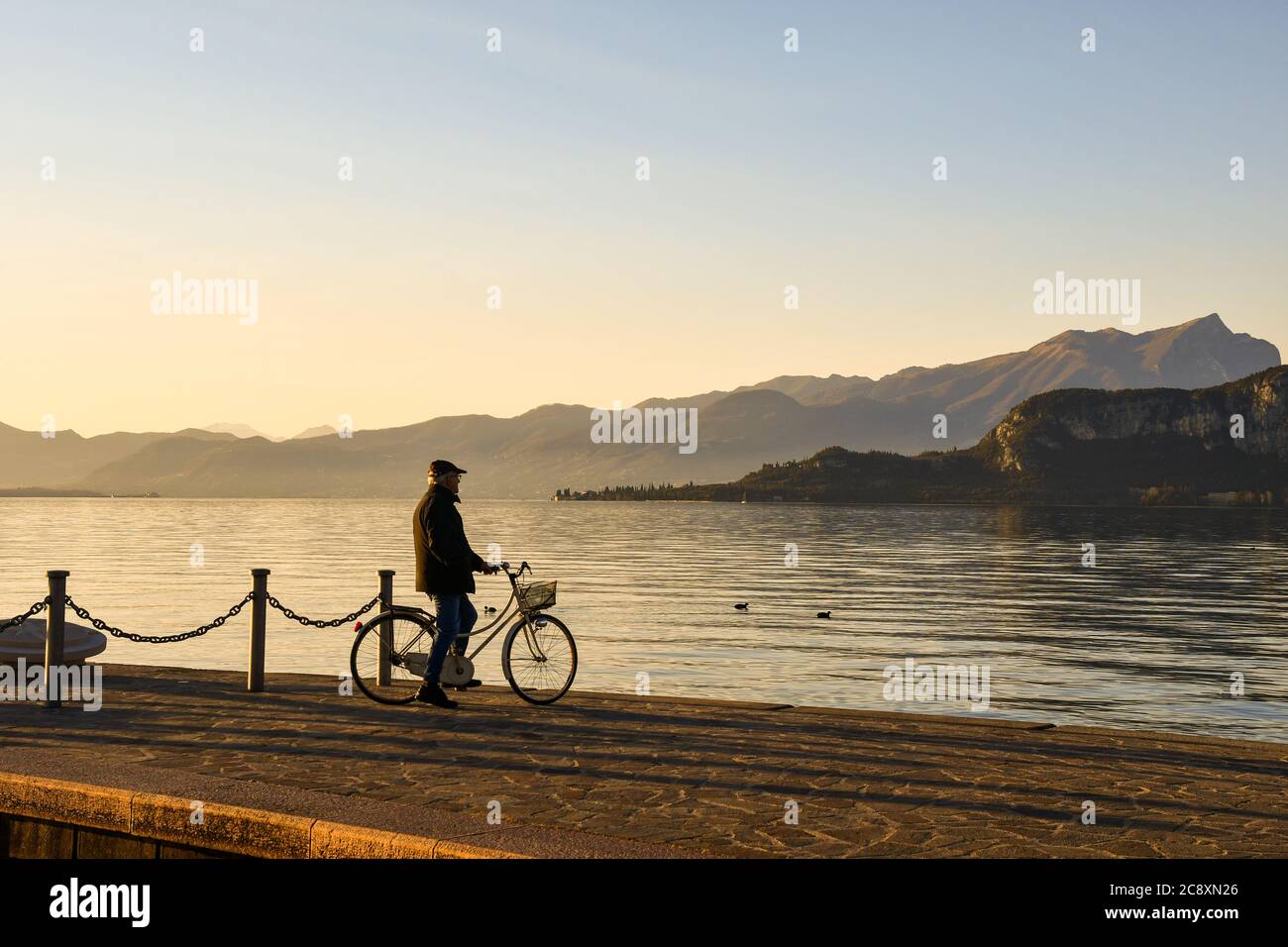 Un anziano in bicicletta che ammira il paesaggio al tramonto sulle sponde del Lago di Garda, Bardolino, Verona, Veneto, Italia Foto Stock
