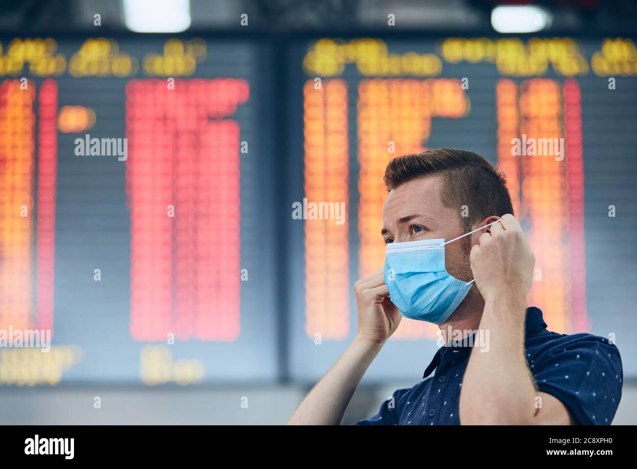 Uomo che indossa una maschera contro il bordo di partenza dell'aeroporto. Temi nuovo normale, coronavirus e protezione personale. Foto Stock