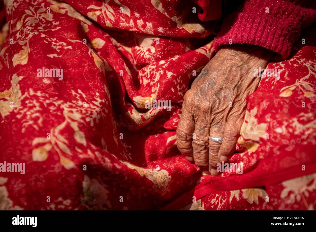 Primo piano dettagli della mano rugosa di una donna nepalese anziana che indossa un abito tradizionale rosso. Nepal Asia Foto Stock