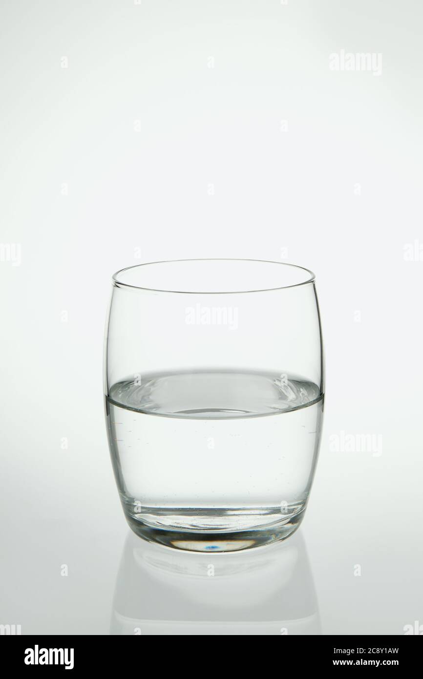 Fotografia di un bicchiere di vetro mezzo pieno d'acqua su uno sfondo chiaro. Foto Stock