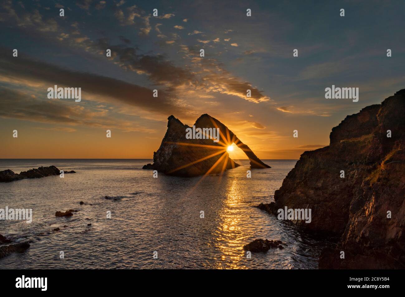 ARCO FIODLE ROCK PORTKNOCKIE MORAY COSTA SCOZIA LUGLIO ALBA CON I RAGGI DEL SOLE CHE PASSANO ATTRAVERSO L'ARCO Foto Stock