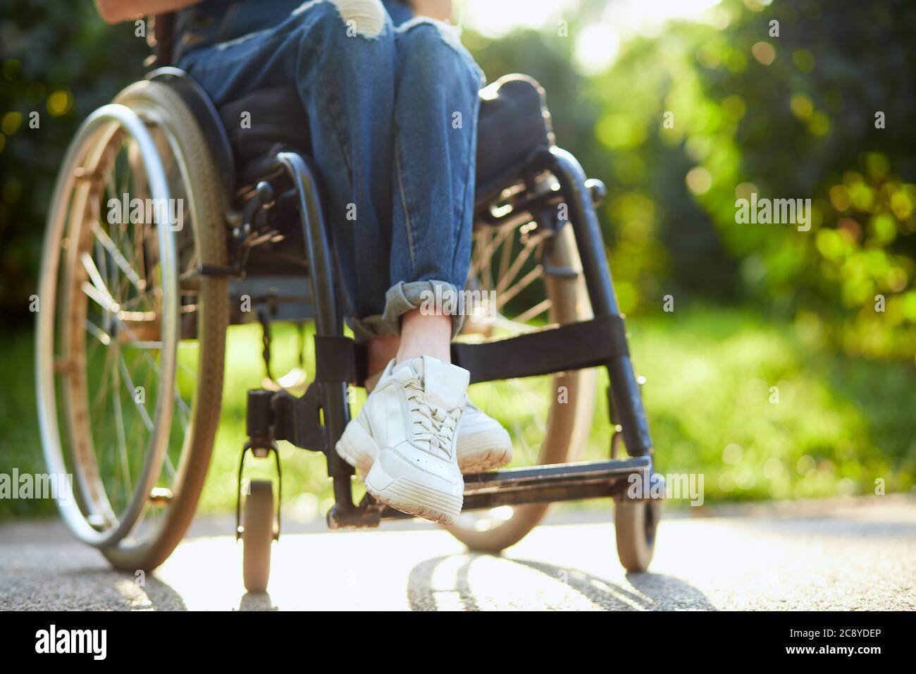 giovane ragazza disabile in tuta e trainer bianchi seduti con gambe incrociate sulla sedia a rotelle. primo piano foto ritagliata. Foto Stock