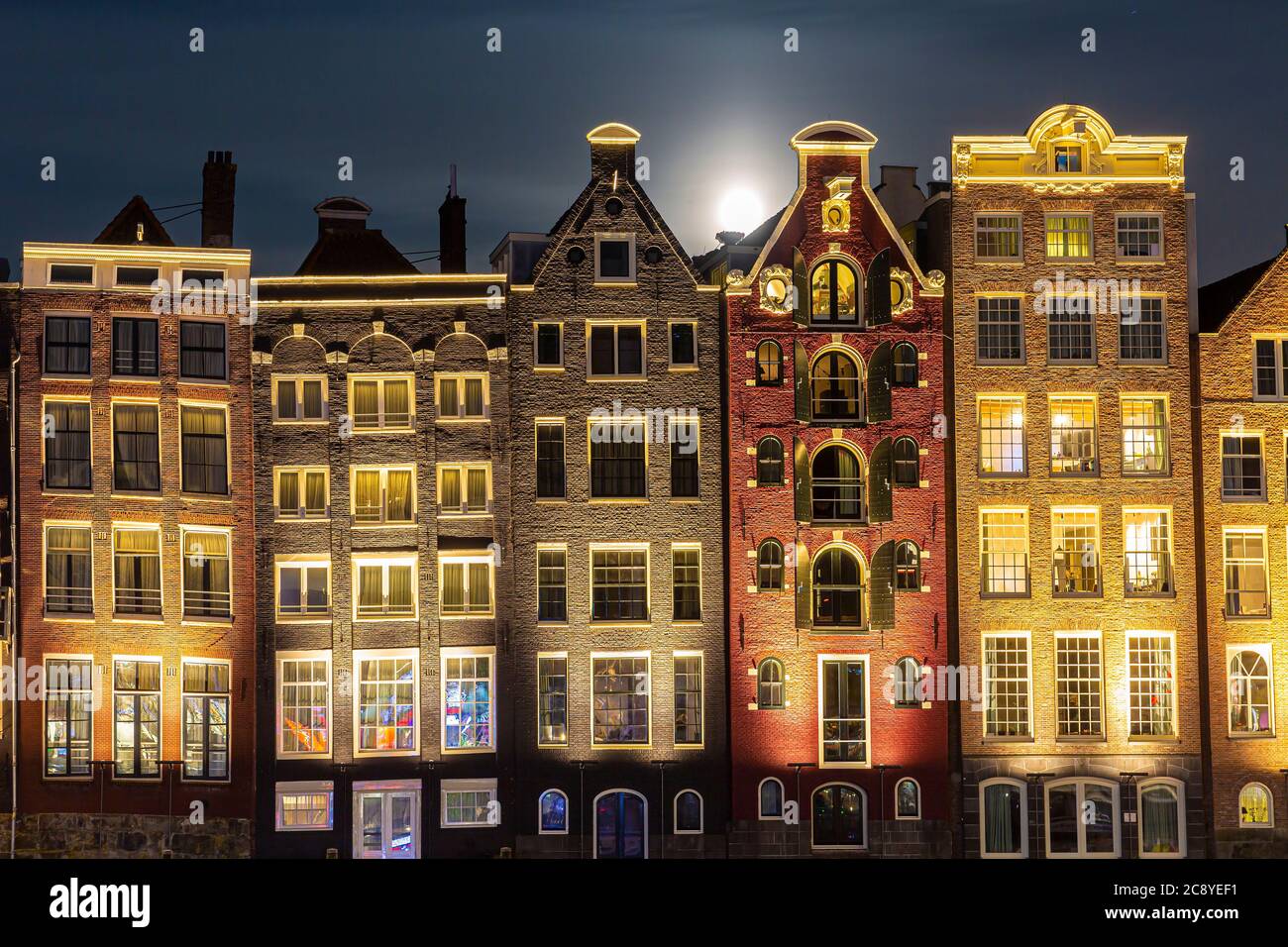 Amsterdam Damrak architettura tradizionale olandese di notte. Tour delle navi da crociera in primo piano. Foto Stock