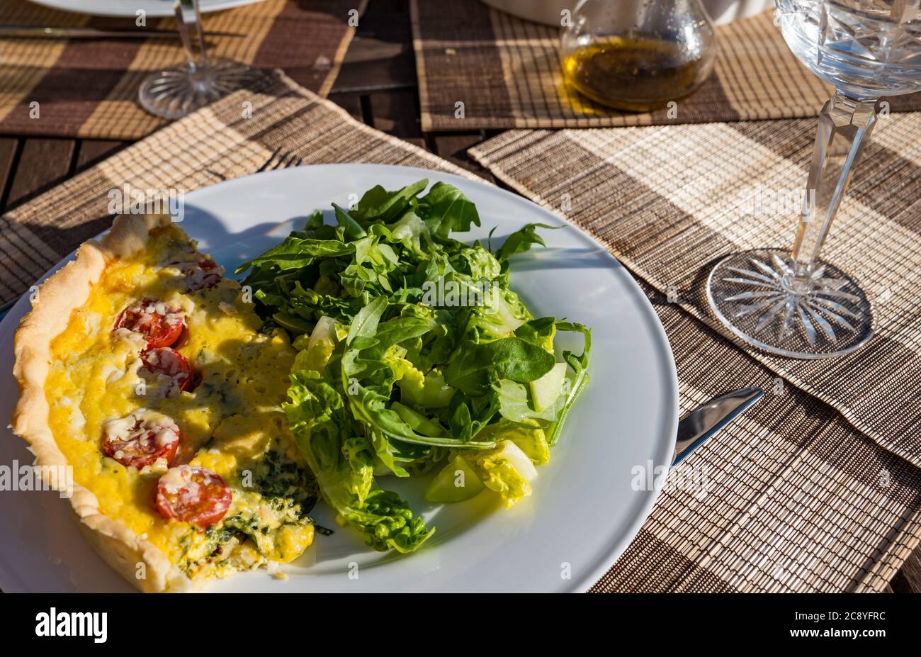 Tavolo esterno pasto estivo di pasticceria di pomodoro e spinaci quiche lorena e insalata verde con bicchiere di vino di cristallo Foto Stock