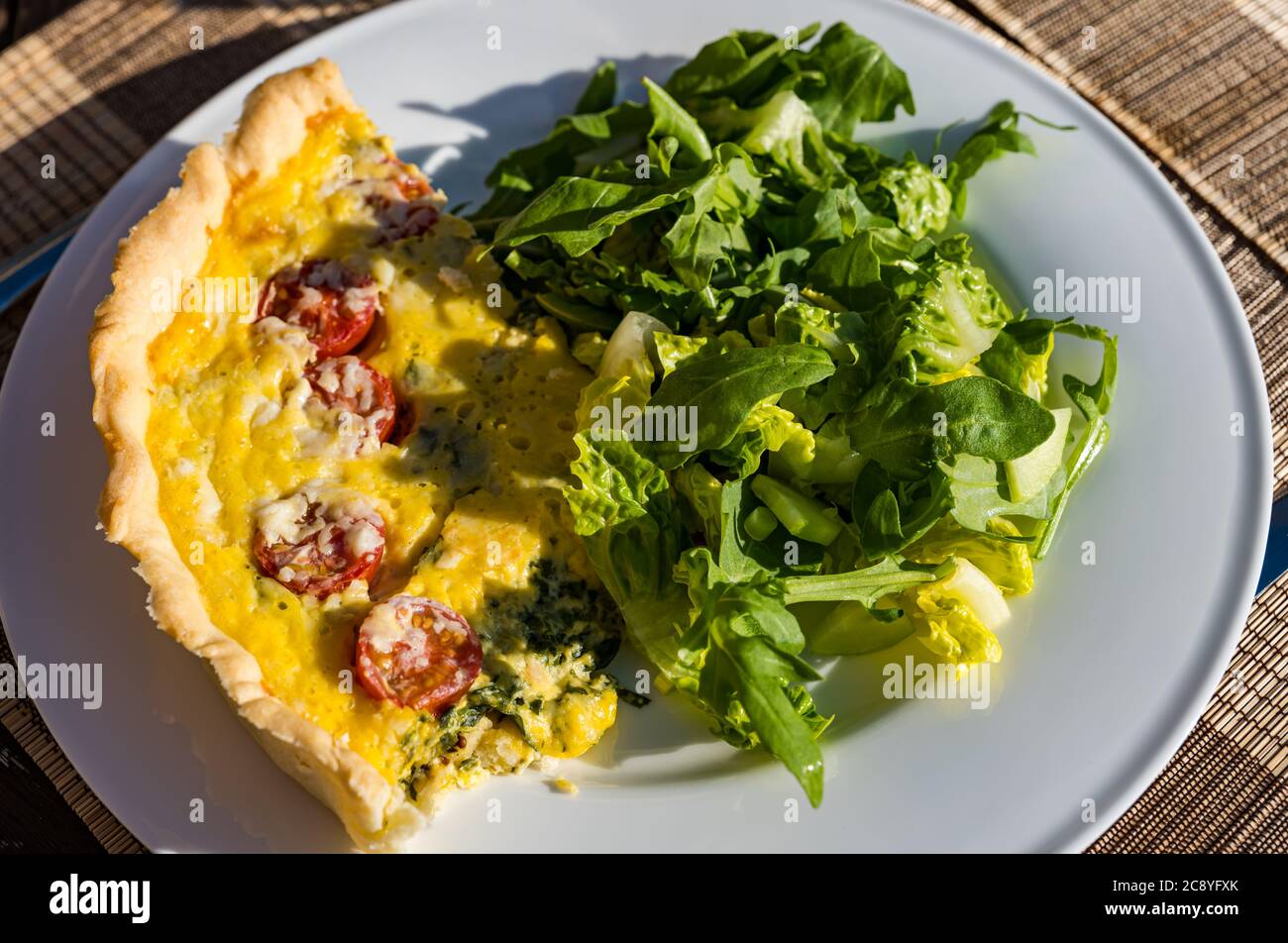 Tavolo esterno con pasto estivo di pomodoro, spinaci e pasta frolla quiche lorena e insalata verde Foto Stock