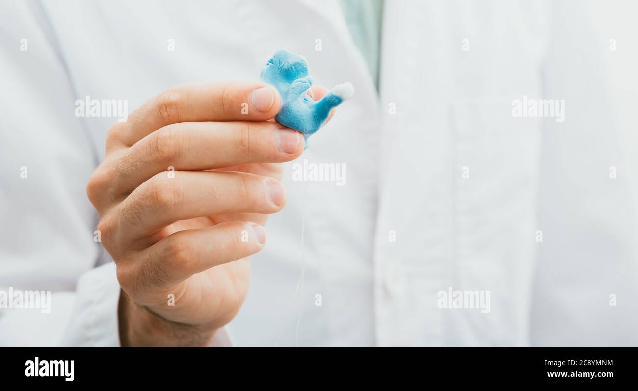 il medico che tiene in mano modellava gli auricolari individuali degli apparecchi acustici per il suo paziente, primo piano. Soluzione per l'udito Foto Stock