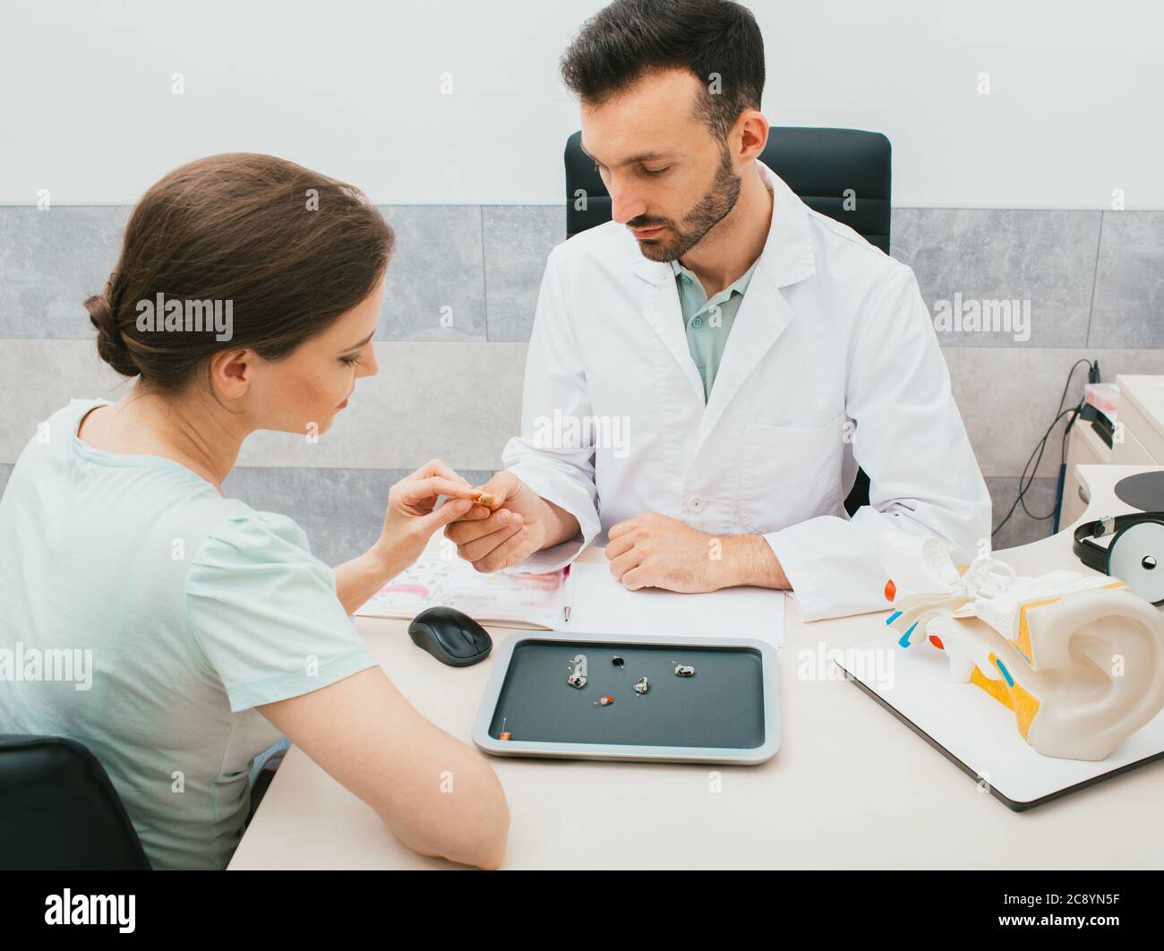 Un giovane audiologo seleziona un apparecchio acustico per una donna caucasica. Il paziente ha bisogno di buoni apparecchi acustici per poter sentire i suoni del mondo. Foto Stock