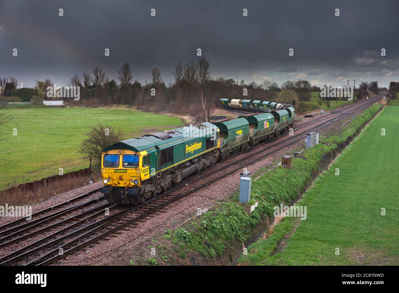 Freightliner classe 66 locomotiva 66614 passando Whitley Bridge Junction, Yorkshire con un treno merci di tramogge inerti vuote con un cielo nero Foto Stock