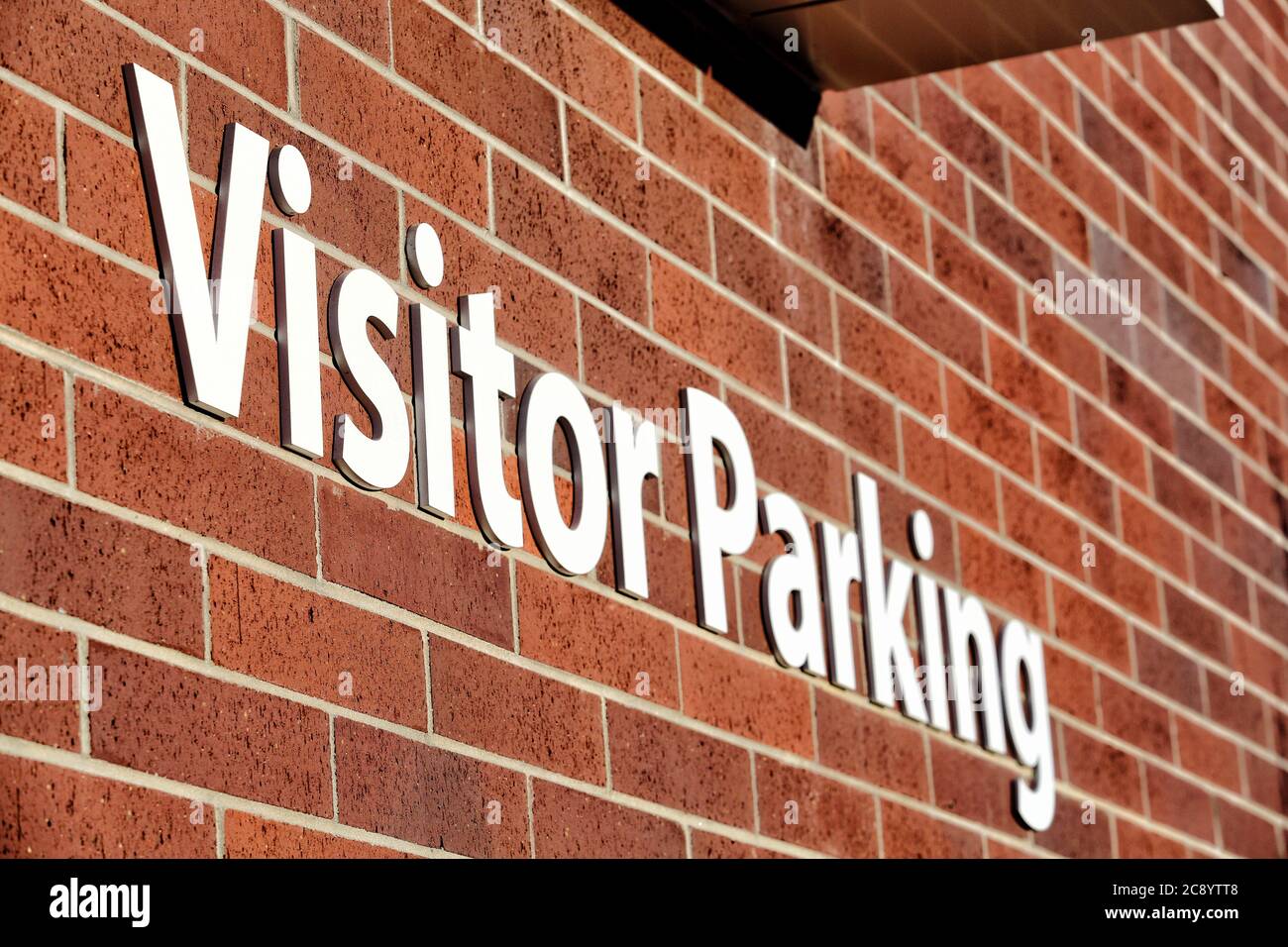 Un cartello bianco in stampatello, su un muro di mattoni rossi, indica ai visitatori un'area parcheggio riservata. Foto Stock