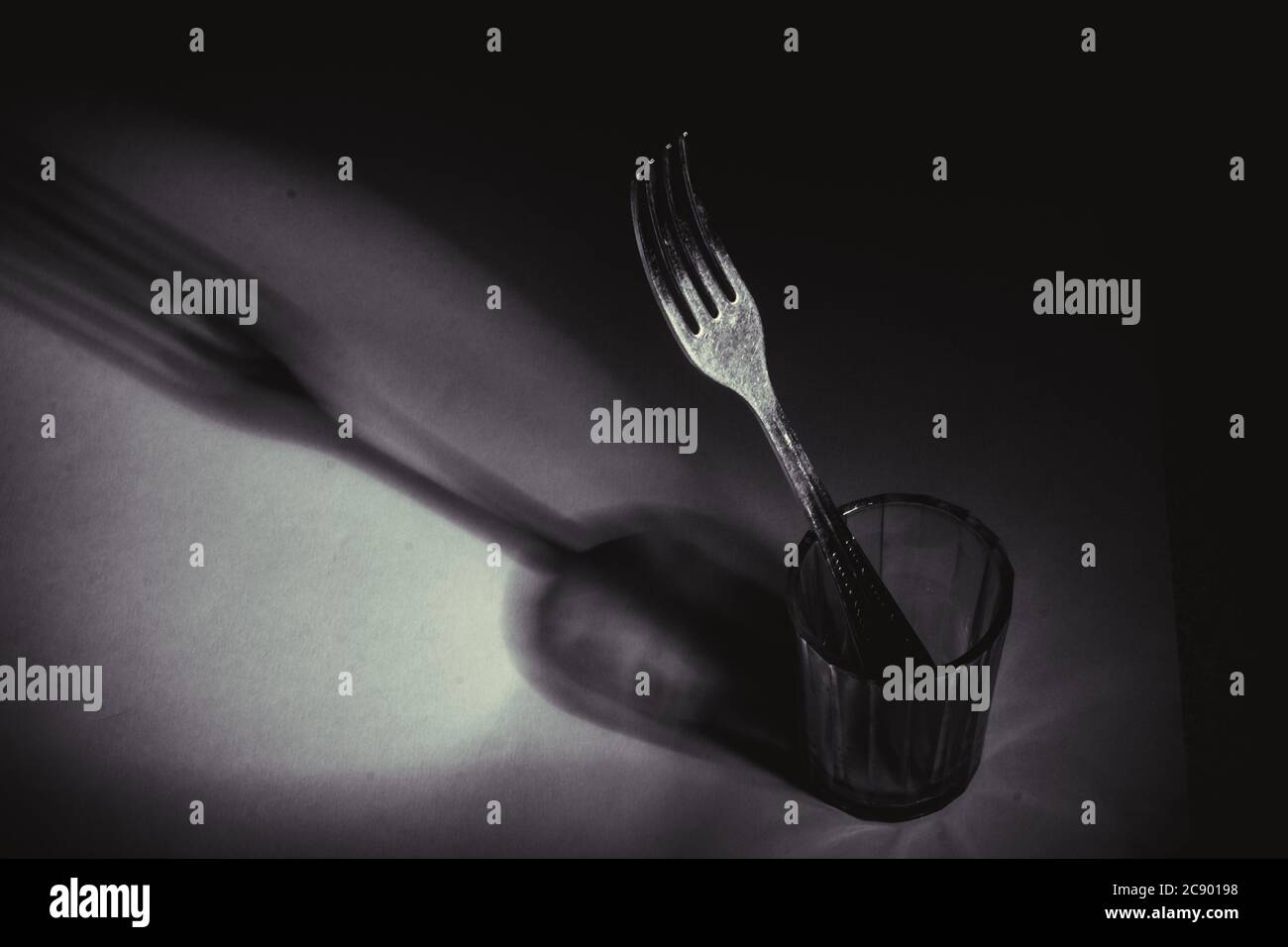 una forchetta in un vetro sfaccettato con bordi su sfondo nero, la sua ombra. Studio Concept photography Foto Stock