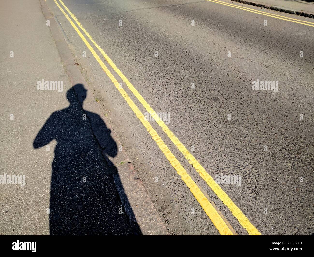 Ombra di figura su Hot Tarmac Asphalt Road con doppie linee gialle Foto Stock
