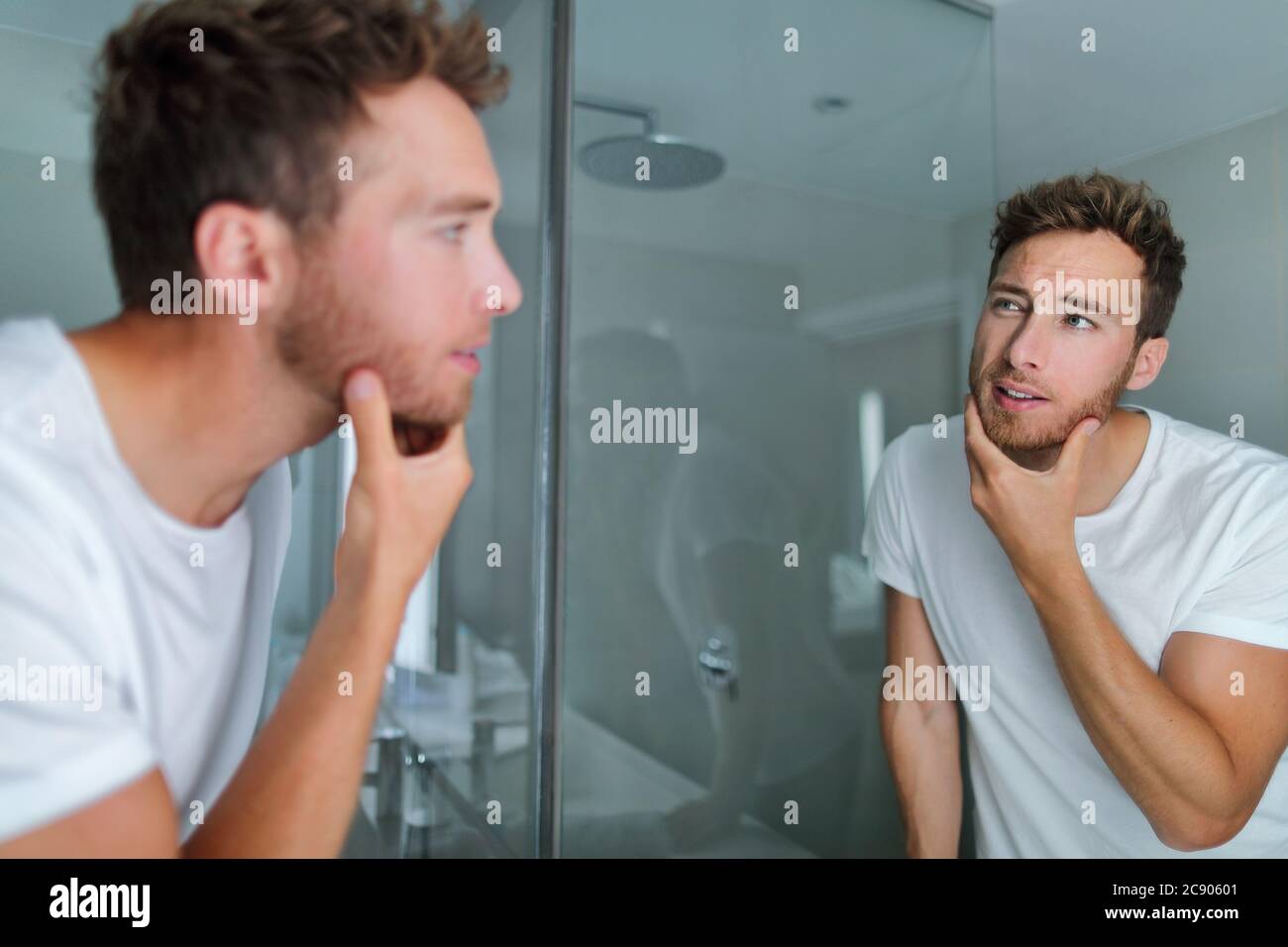 L'uomo si faccia cura guardando nello specchio che tocca la sua barba o la salute della pelle. Maschile bellezza mattina cura della pelle routine in bagno casa. Dopo la rasatura degli uomini Foto Stock