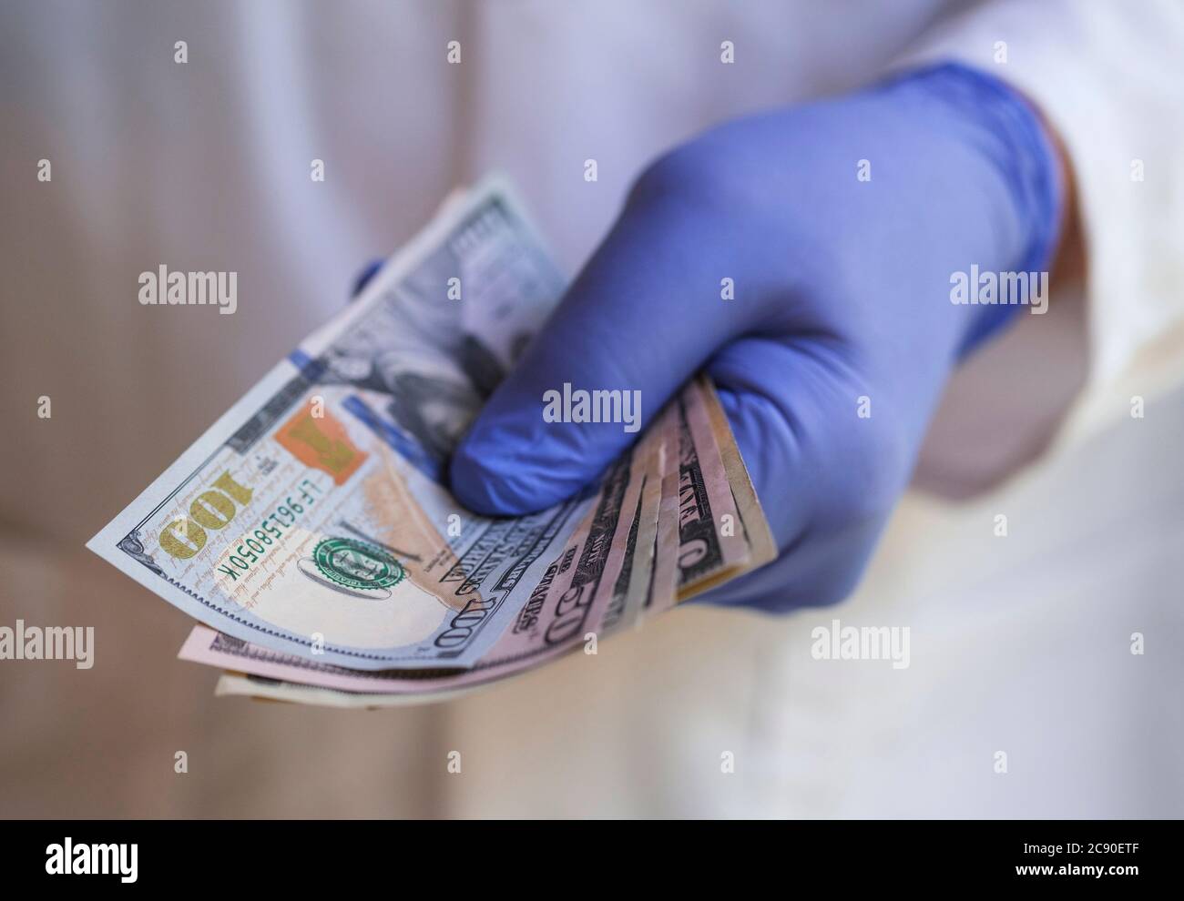 Persona in guanto chirurgico che tiene i soldi Foto Stock