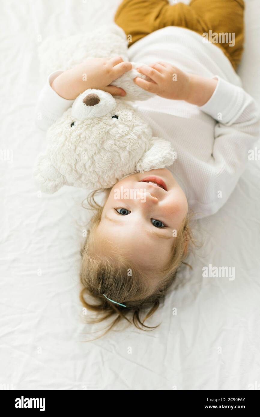 Bambina sorridente sdraiata sul letto con il giocattolo dell'orsacchiotto Foto Stock Bambina sorridente sdraiata sul letto con il giocattolo dell'orsacchiotto Foto Stock