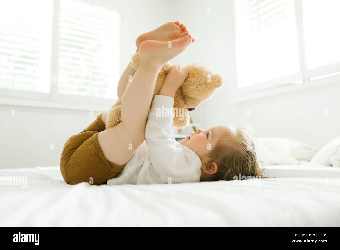 Bambina sdraiata sul letto con il suo giocattolo da orsacchiotto Foto Stock