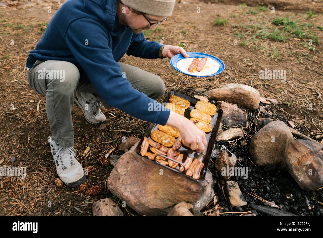 Uomo che cucina prima colazione durante il campeggio Foto Stock