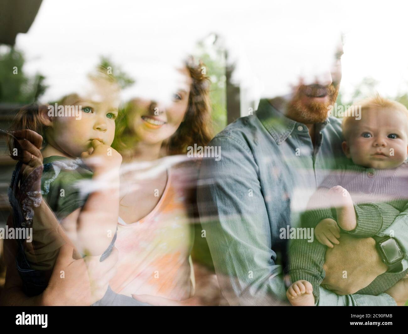 Famiglia con bambini (6-11 mesi, 2-3) che guardano attraverso la finestra Foto Stock