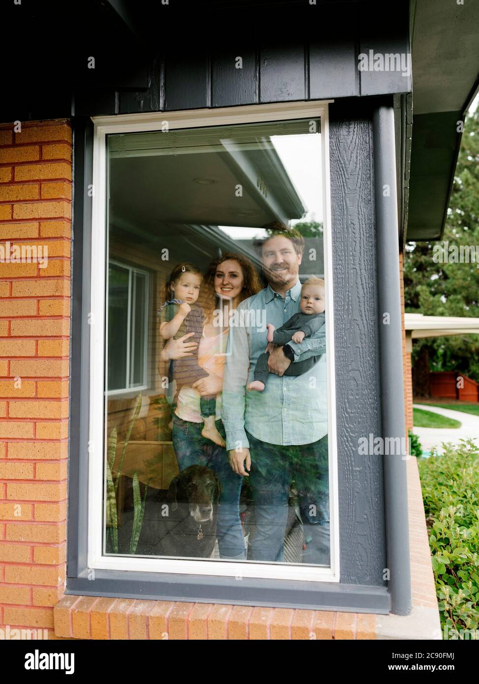 Famiglia con bambini (6-11 mesi, 2-3) che guardano attraverso la finestra Foto Stock