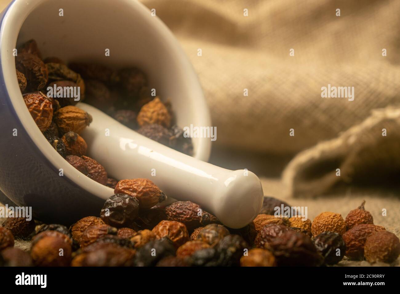 Frutta secca di rosa canina in un mortaio di ceramica e frutta secca di rosa canina sparsa su un panno di casa con una consistenza ruvida. Primo piano Foto Stock