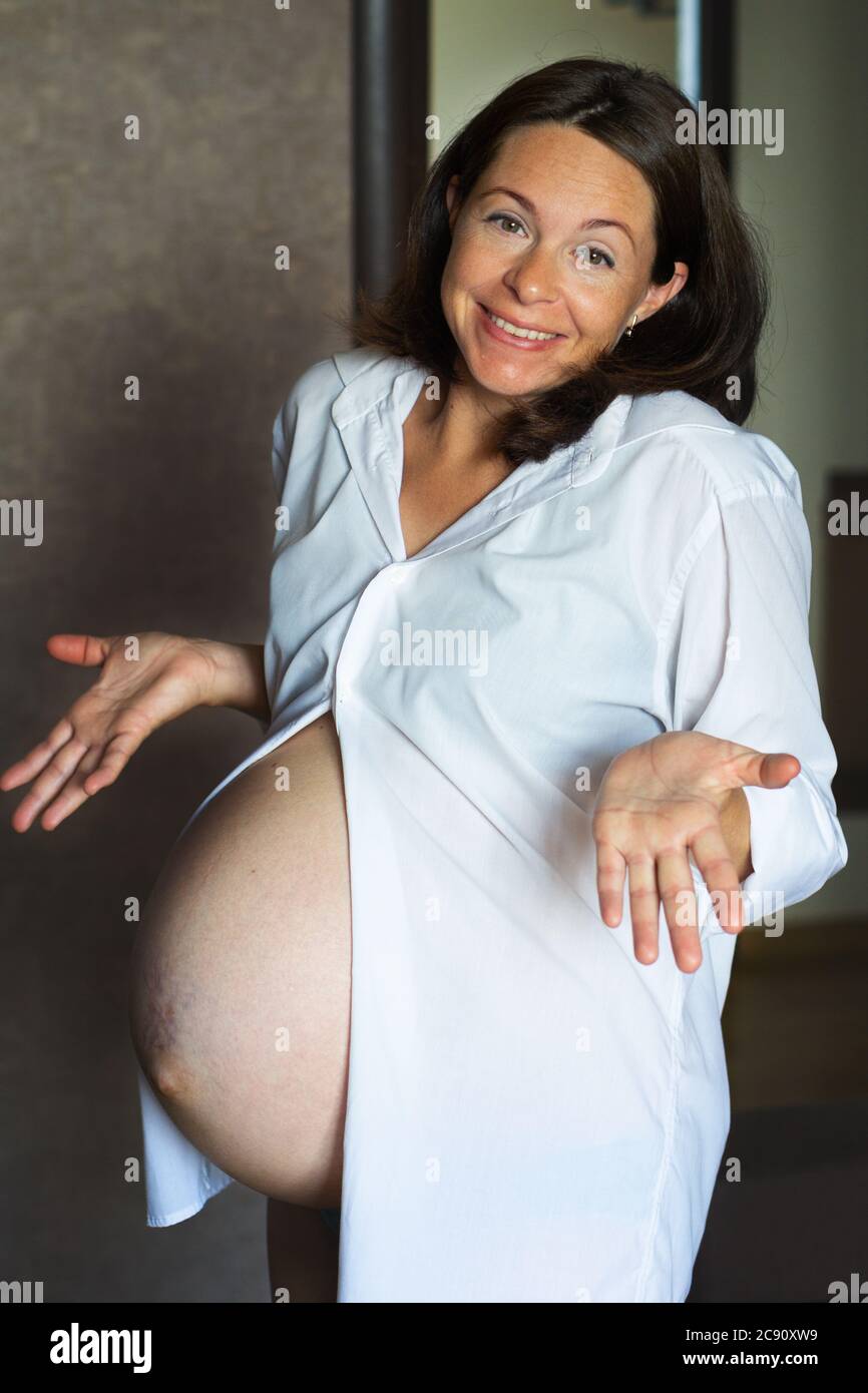 Ritratto di felice donna incinta di mezza età in una camicia bianca da uomo sorride e si diffonde le mani. Concetto di felicità sana gravidanza e. Foto Stock