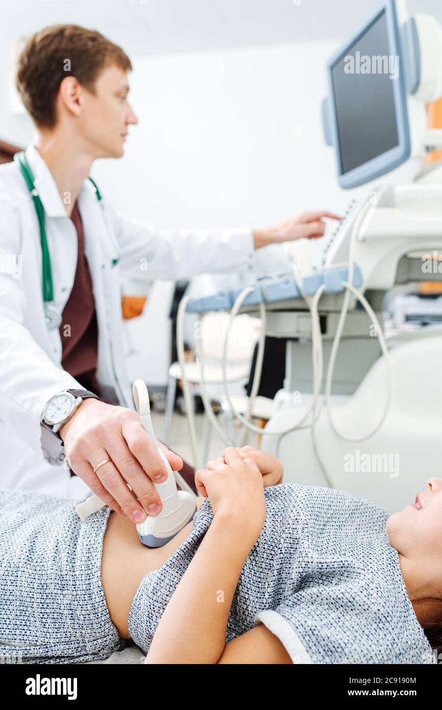 La mano del medico che muove la sonda ecografica su uno stomaco della ragazza di dieci anni Foto Stock