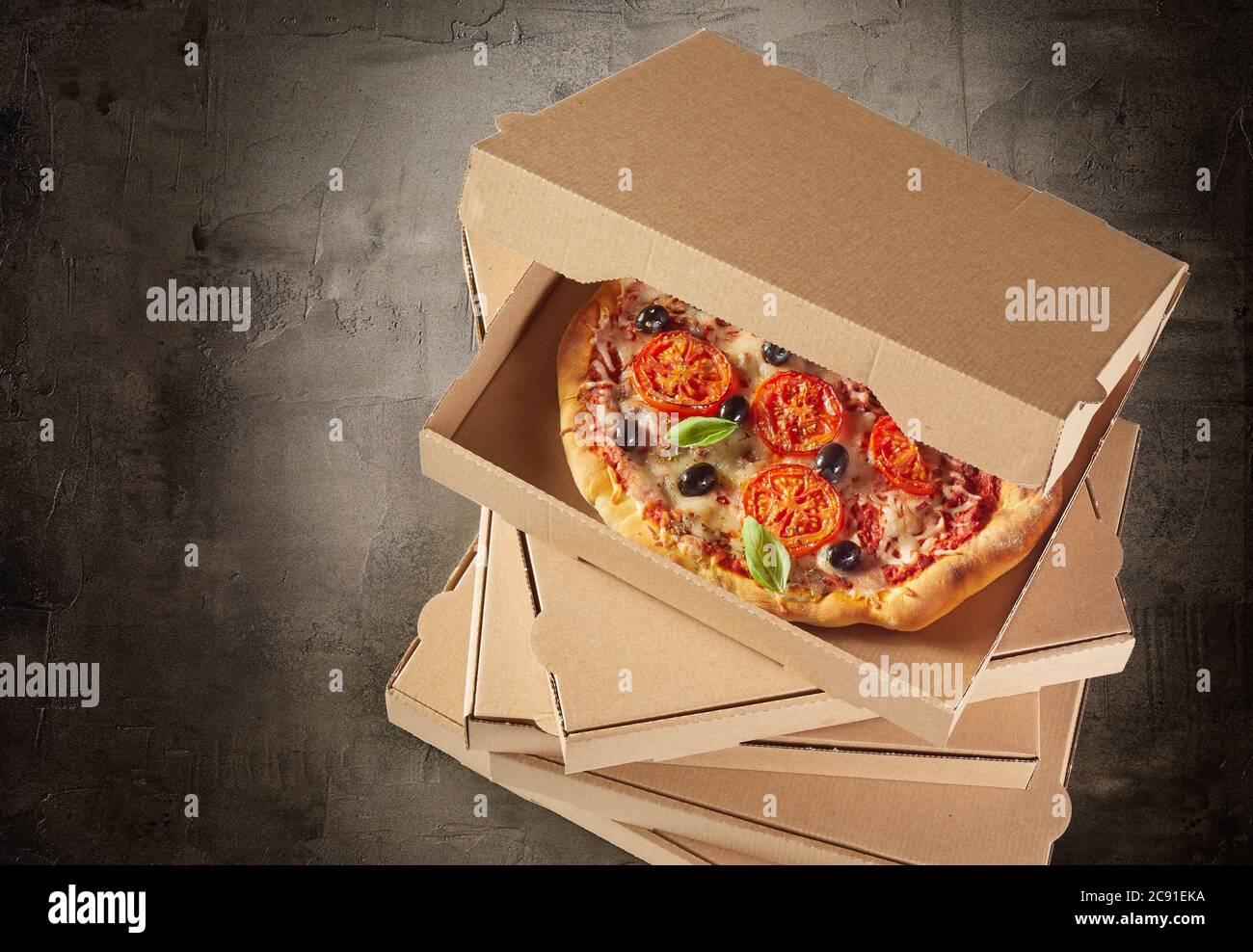 Scatole di cartone marrone generico impilate con una gustosa pizza fresca italiana all'interno della scatola aperta vista dall'alto su ardesia con vignetta Foto Stock