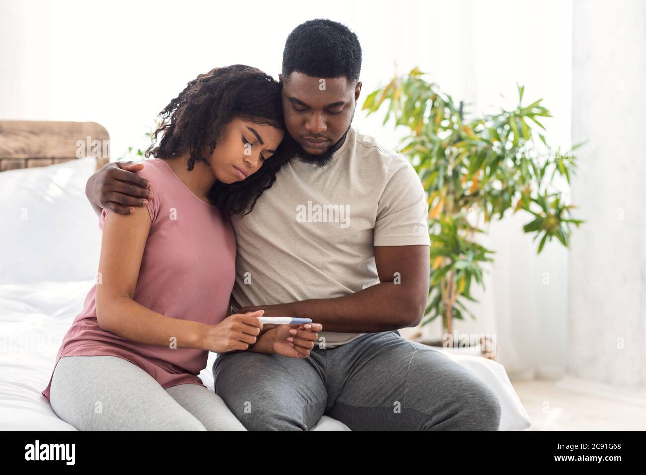 African triste ragazzo abbracciando sua moglie che tiene negativo test di gravidanza Foto Stock