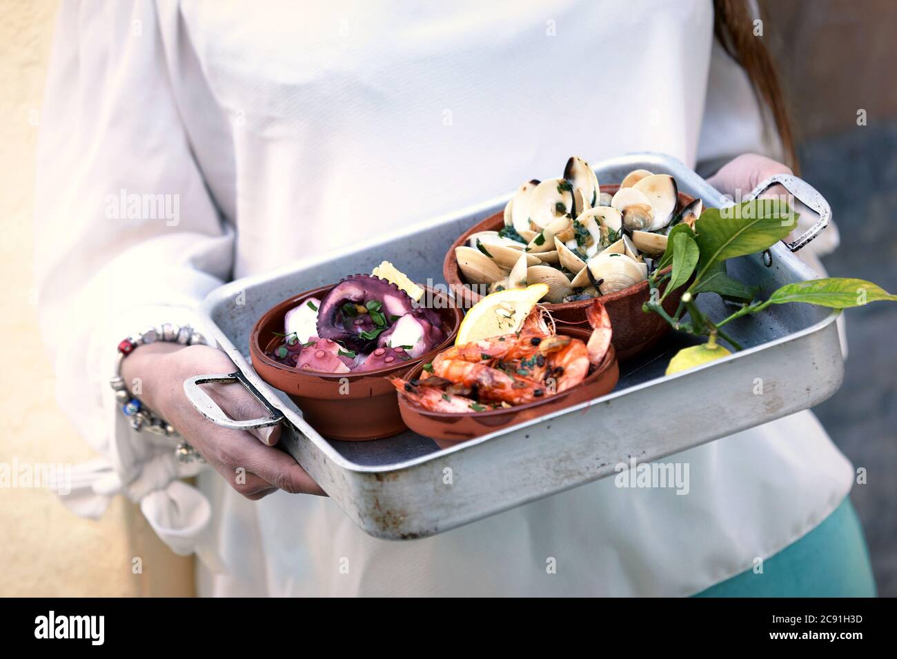 Donna che porta un assortimento di piatti di pesce in un piccolo vassoio di metallo con gamberi alla griglia e vongole salate da vicino Foto Stock