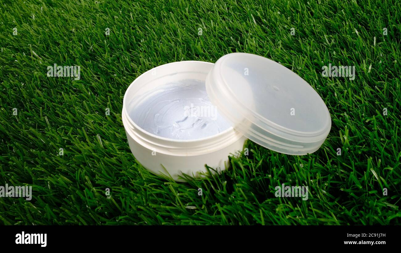 bellezza, vaso bianco con scrub corpo su fondo verde erba primo piano. cosmetici per la cura della pelle. Foto Stock