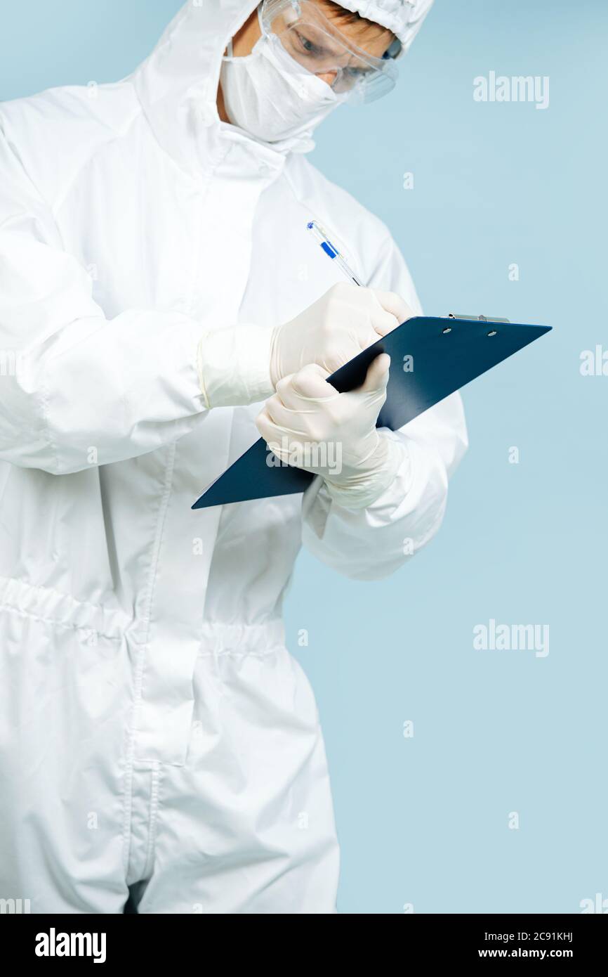 Medico in un costume bianco che copre tutta la pelle di scrittura su cartella di plastica Foto Stock