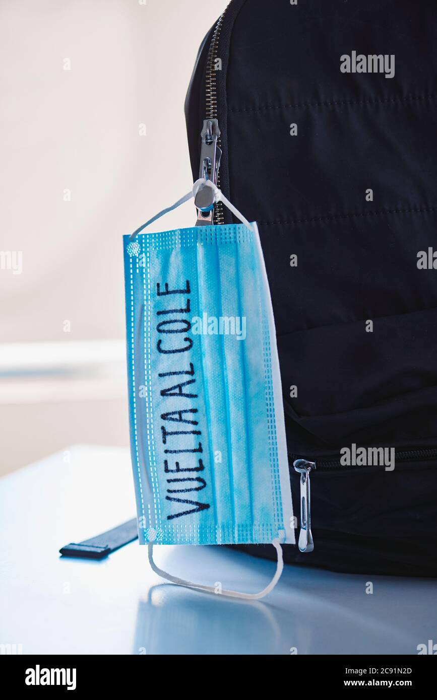 chiusura di un bookbag nero e di una maschera chirurgica blu con il testo di ritorno a scuola scritto in spagnolo, che raffigura la necessità di prevenire l'infezione a sc Foto Stock