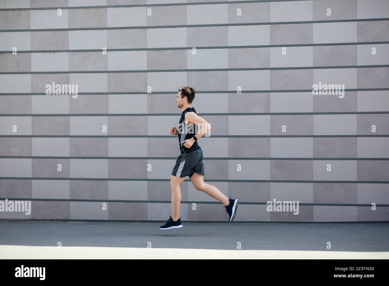 Atleta e jogging al mattino. Ragazzo muscolare in abbigliamento sportivo e fitness tracker, corre Foto Stock