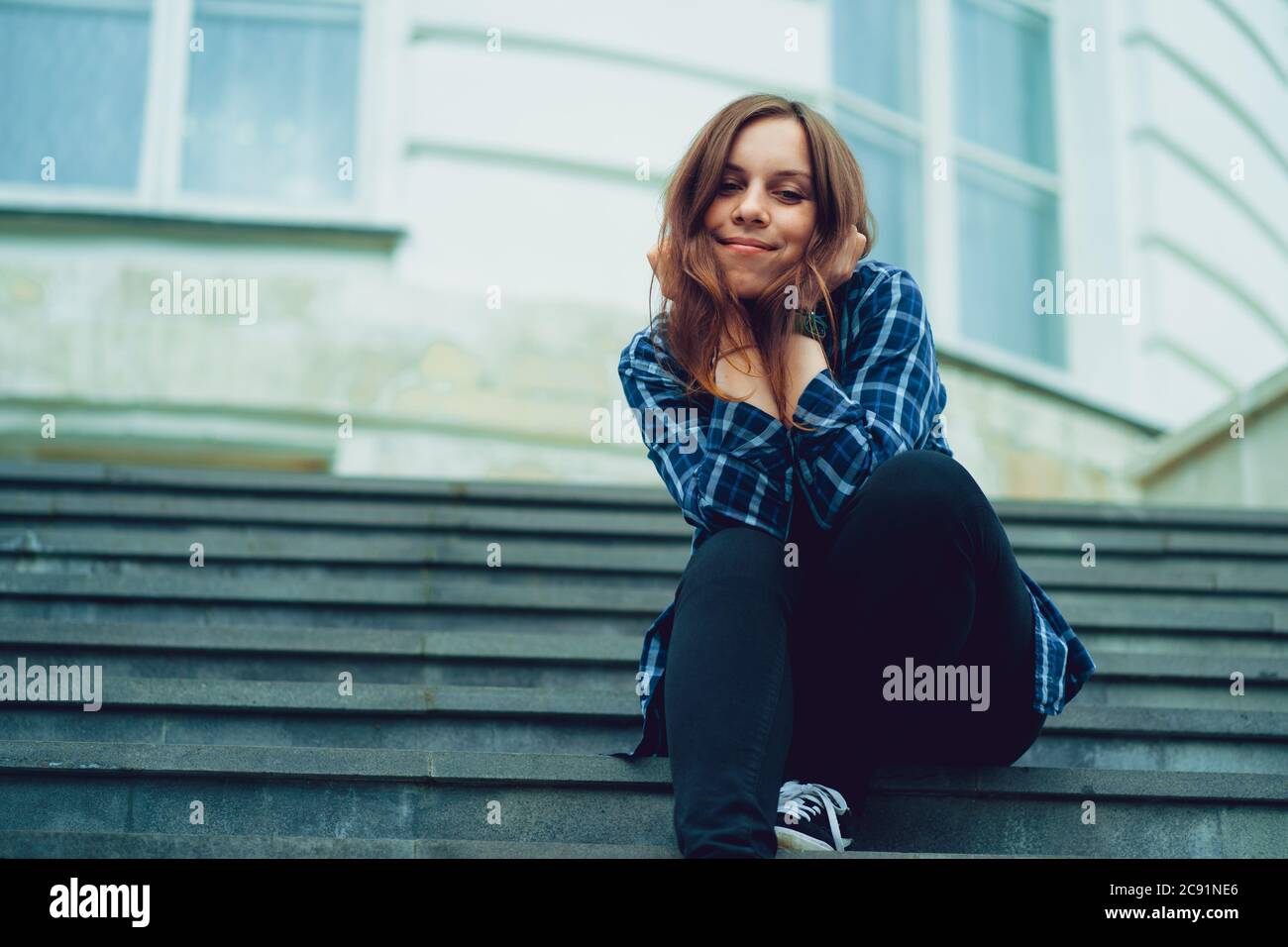 Giovane bella donna posa su scale di maniero. Donna sorridente adulta seduta sui gradini del palazzo. Foto Stock