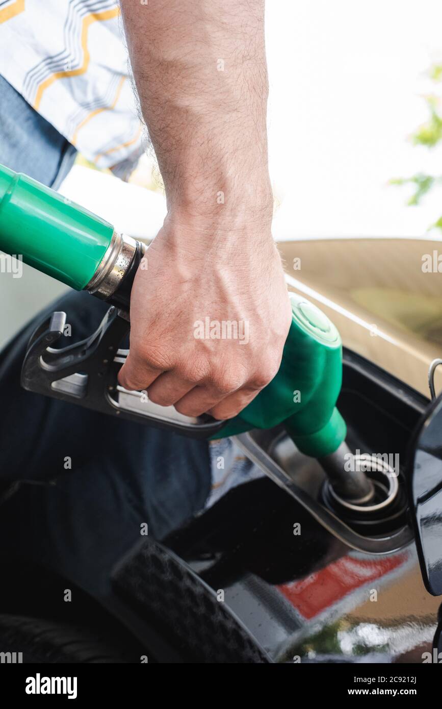 Vista tagliata dell'uomo che tiene l'ugello di rifornimento vicino al coperchio del serbatoio del gas aperto all'esterno Foto Stock