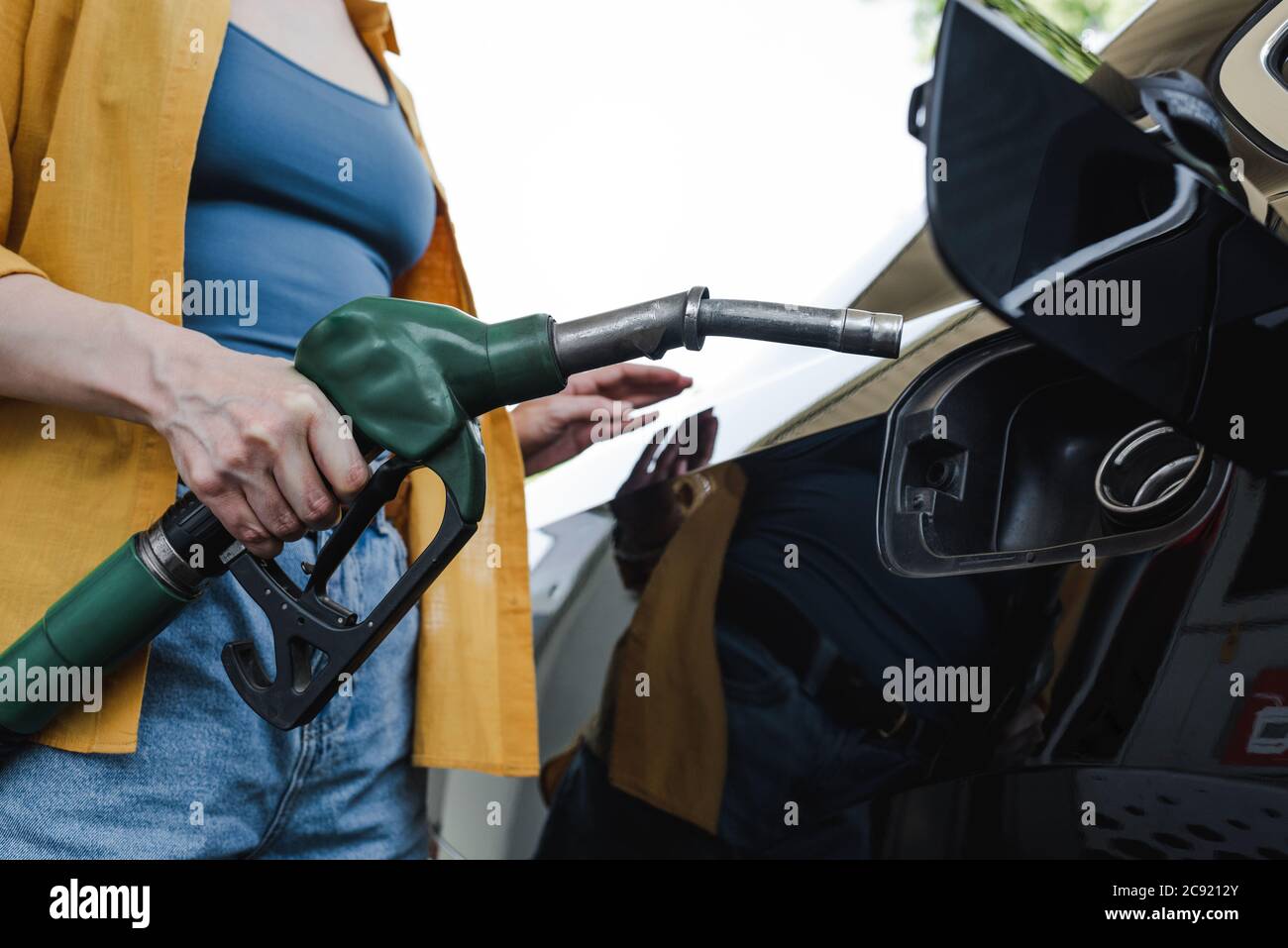 Vista ritagliata della donna che tiene la pistola di rifornimento vicino alla stazione di servizio automatica Foto Stock