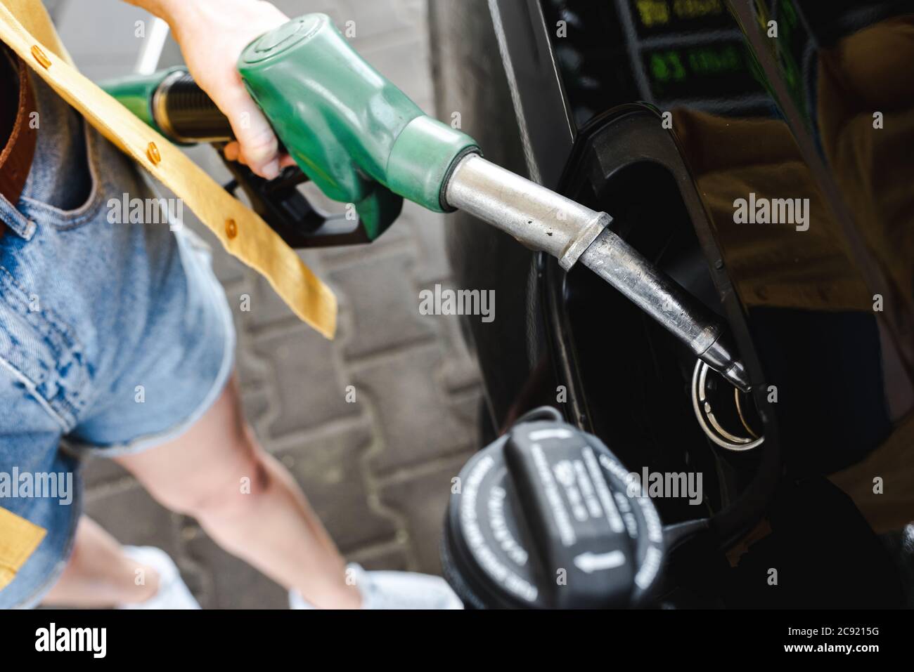 Vista tagliata della donna che tiene la bocchetta di rifornimento vicino all'auto sulla stazione di servizio Foto Stock