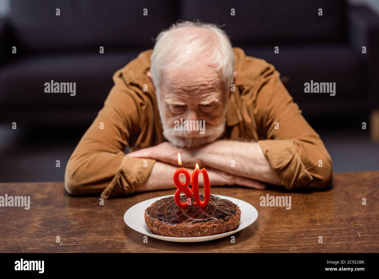 uomo solitario anziano che guarda la torta di compleanno con il numero ottanta Foto Stock