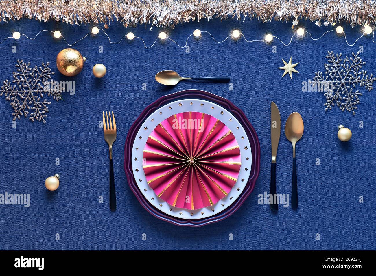 Tavolo di Natale in bianco, oro, borgogna con posate nere e dorate, su tovaglia di lino blu scuro Foto Stock