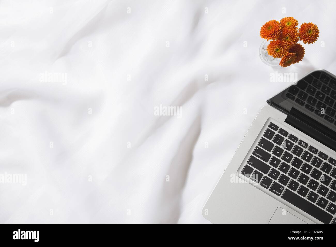 Vista dall'alto dello sfondo in tessuto voile con un computer portatile e un vaso di fiori arancioni con spazio per il testo Foto Stock