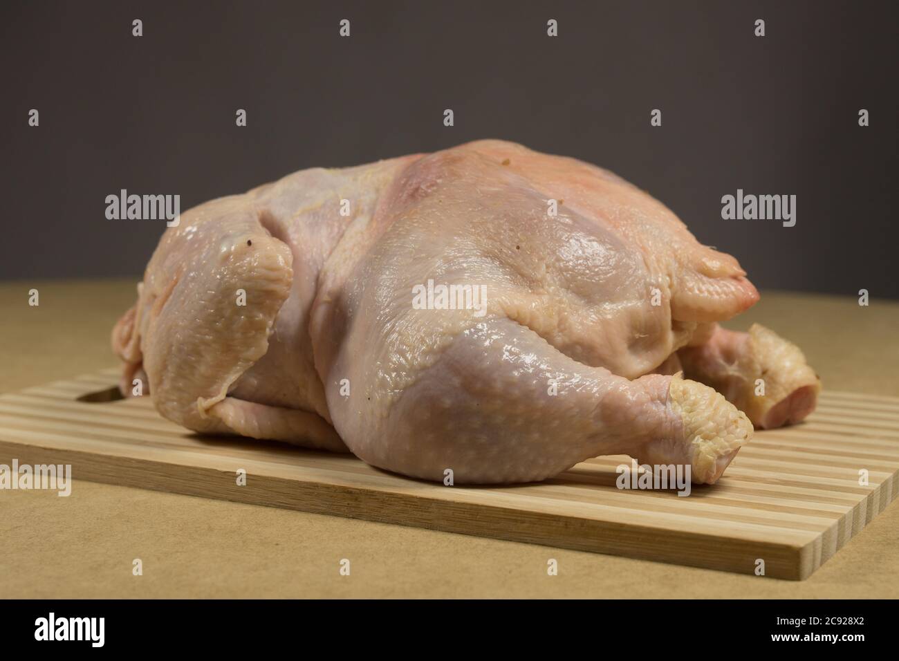 Carcassa di pollo cruda con spezie ed erbe su un tagliere su un tavolo di legno Foto Stock