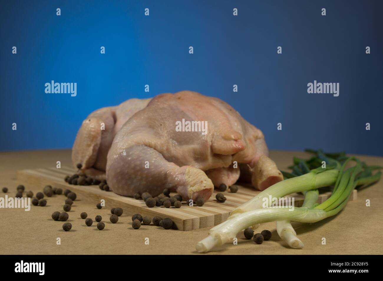 Carcassa di pollo cruda con spezie ed erbe su un tagliere su un tavolo di legno Foto Stock