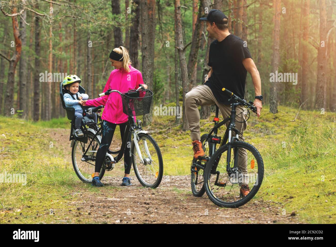 famiglia giovane in bicicletta su sentiero forestale con bambino in bicicletta seggiolino per bambini. sport attivi attività ricreative all'aperto Foto Stock
