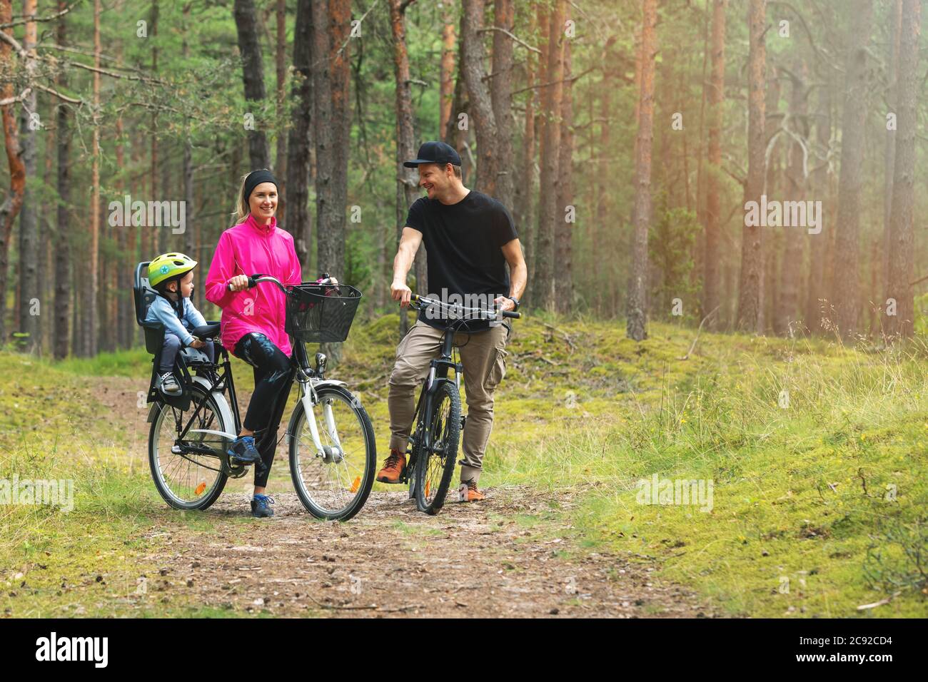 famiglia giovane in bicicletta su sentiero forestale con bambino in bicicletta seggiolino per bambini. sport attivi attività ricreative all'aperto Foto Stock