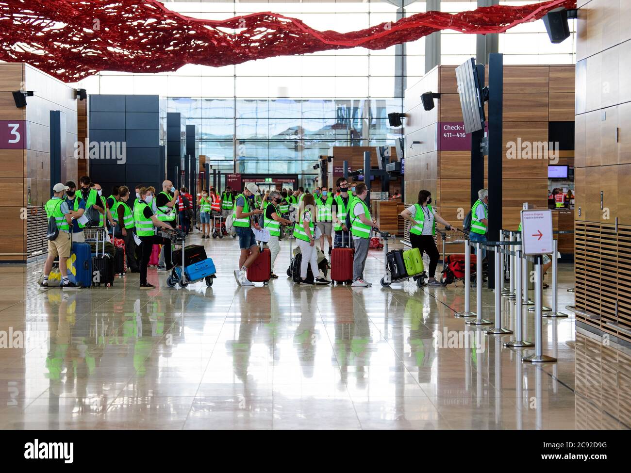 28 luglio 2020, Brandenburg, Schönefeld: Extra in giubbotti verdi ad alta visibilità attendere il check-in durante la prova al Terminal 1 dell'aeroporto capitale Berlino-Brandeburgo (BER). Nella seconda fase del trasferimento operativo e di aeroporto (ORAT), circa 500 - 600 dipendenti aeroportuali e 400 volontari hanno provato le procedure standard per i passeggeri, dal check-in al controllo di sicurezza, dall'imbarco al sbarco (arrivo). Foto: Soeren Stache/dpa-Zentralbild/dpa Foto Stock