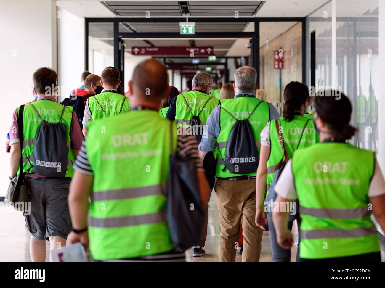 28 luglio 2020, Brandenburg, Schönefeld: Extra in giubbotti verdi ad alta visibilità lasciano il terminal durante la prova all'aeroporto di Berlino-Brandeburgo (BER) dopo il loro primo arrivo. Nella seconda fase del trasferimento operativo e di aeroporto (ORAT), circa 500 - 600 dipendenti e 400 volontari hanno provato le procedure standard per i passeggeri, dal check-in al controllo di sicurezza fino all'imbarco e al deboarding (arrivo). Foto: Soeren Stache/dpa-Zentralbild/dpa Foto Stock