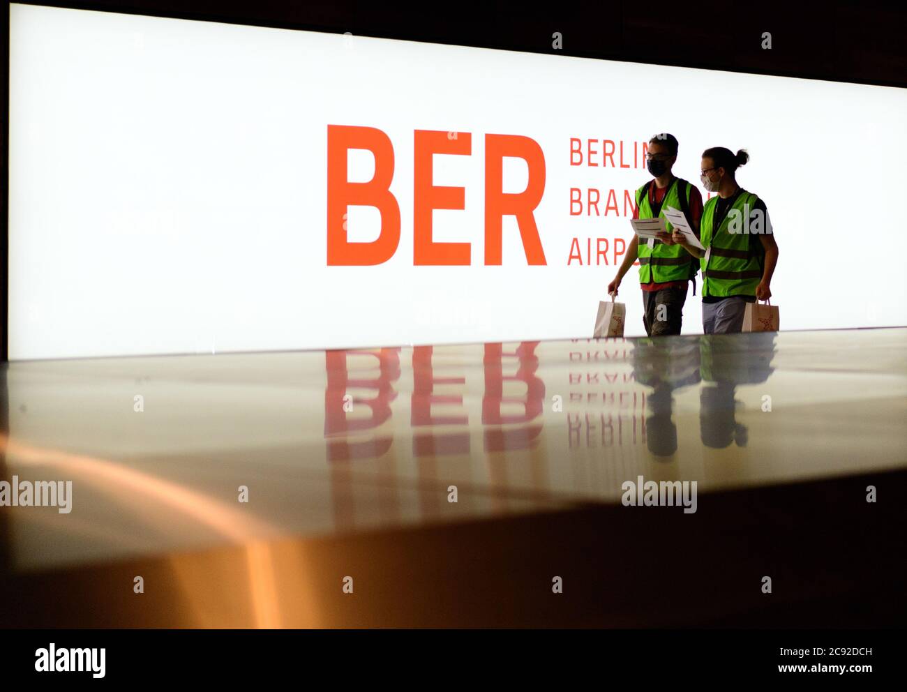 28 luglio 2020, Brandenburg, Schönefeld: Gli extra in giubbotti verdi ad alta visibilità vanno al carosello bagagli nel Terminal 1 dell'aeroporto di Berlino-Brandeburgo (BER) per ritirare le valigie durante la corsa di prova prima del check-in. Nella seconda fase del trasferimento operazionale e di aeroporto (ORAT), circa 500 - 600 dipendenti e 400 volontari hanno provato le procedure standard per i passeggeri, dal check-in al controllo di sicurezza, dall'imbarco e dal sbarco (arrivo). Foto: Soeren Stache/dpa-Zentralbild/dpa Foto Stock