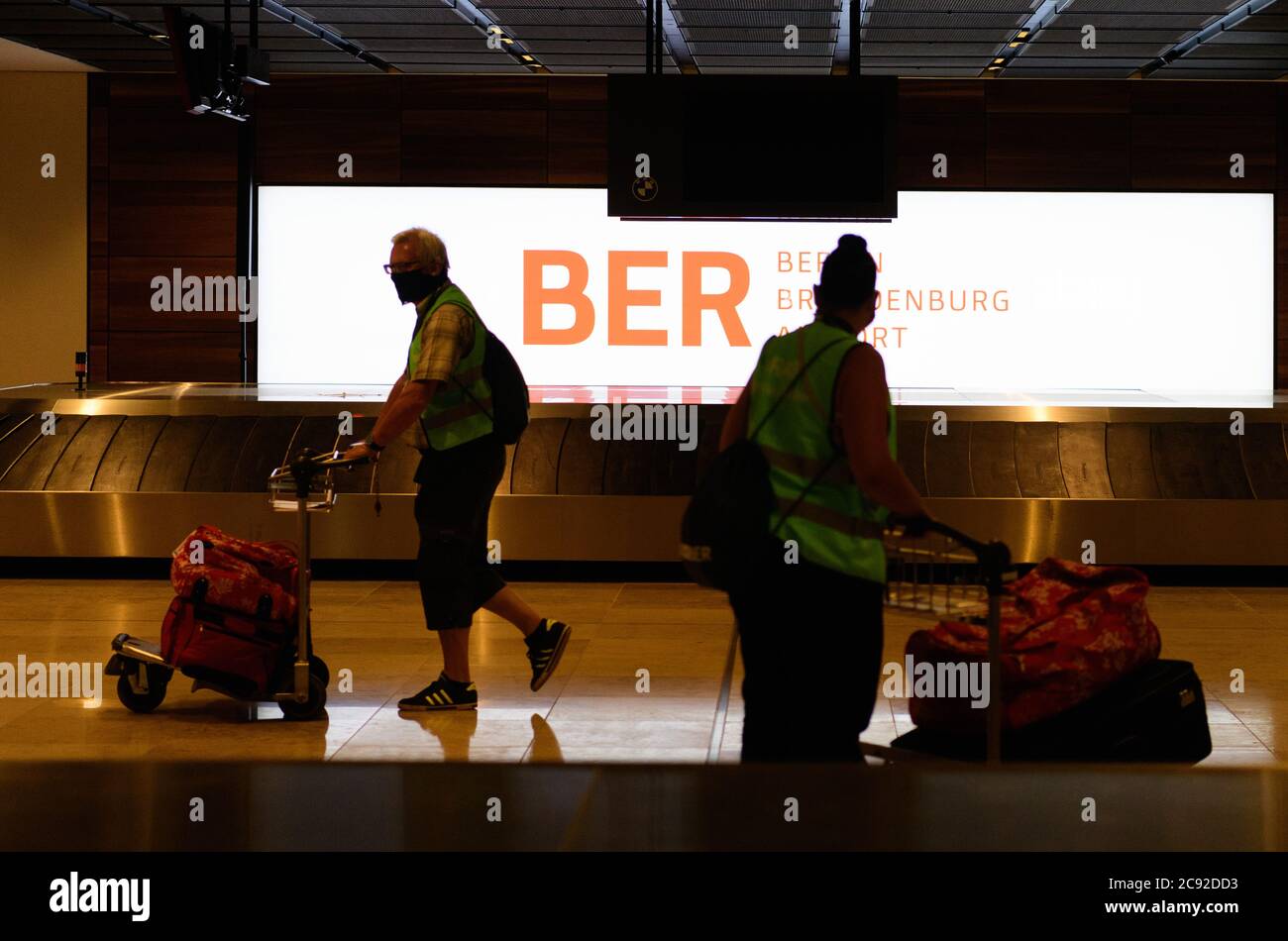 28 luglio 2020, Brandenburg, Schönefeld: Extra in giubbotti verdi ad alta visibilità vanno in valigie per il check-in durante la prova di prova nel Terminal 1 dell'aeroporto capitale Berlino-Brandeburgo (BER). Nella seconda fase del trasferimento operazionale e di aeroporto (ORAT), circa 500 - 600 dipendenti e 400 volontari hanno provato le procedure standard per i passeggeri, dal check-in al controllo di sicurezza, dall'imbarco e dal sbarco (arrivo). Foto: Soeren Stache/dpa-Zentralbild/dpa Foto Stock
