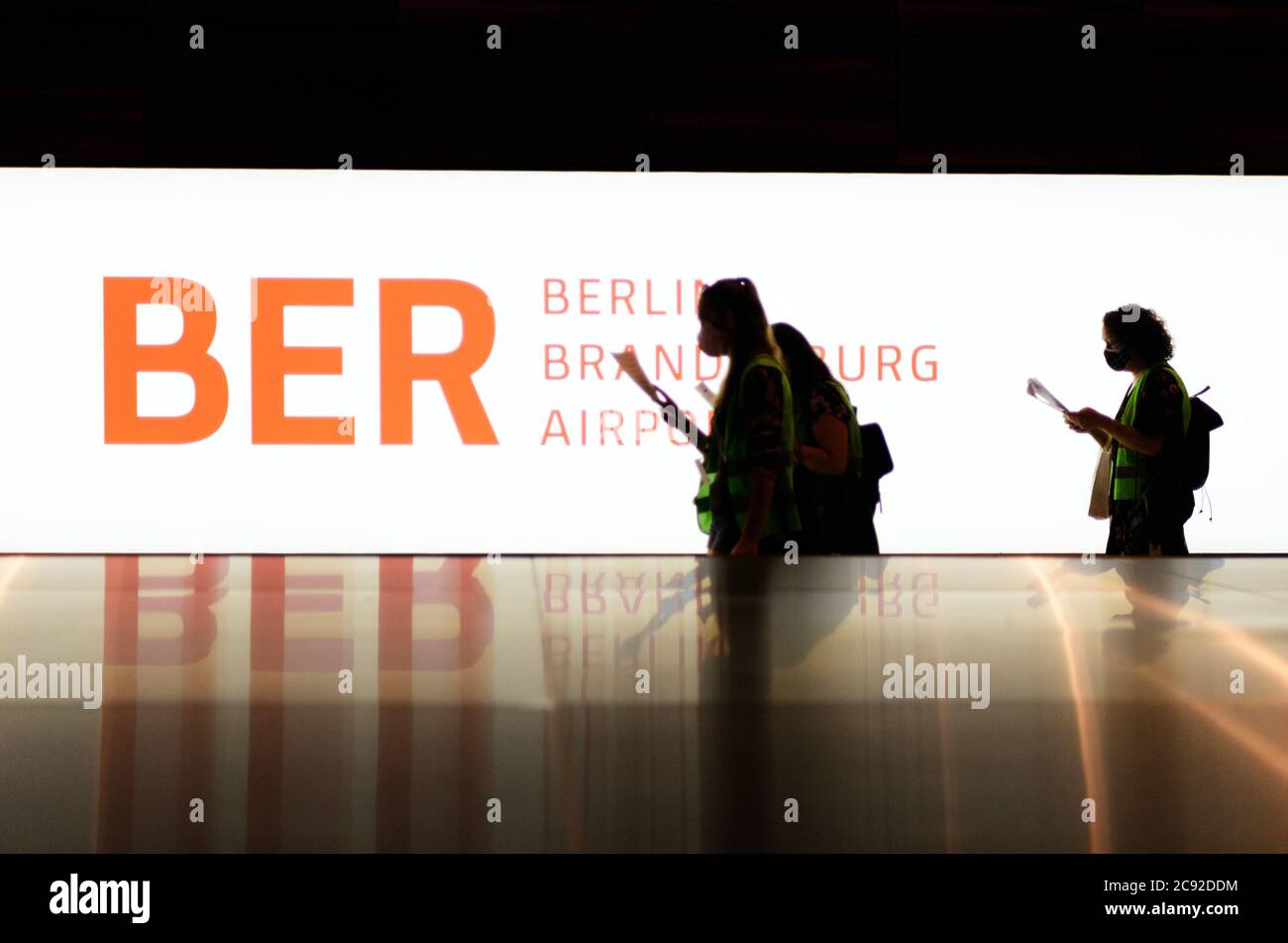 28 luglio 2020, Brandenburg, Schönefeld: Gli extra in giubbotti verdi ad alta visibilità vanno al carosello bagagli nel Terminal 1 dell'aeroporto di Berlino-Brandeburgo (BER) per ritirare le valigie durante la corsa di prova prima del check-in. Nella seconda fase del trasferimento operazionale e di aeroporto (ORAT), circa 500 - 600 dipendenti e 400 volontari hanno provato le procedure standard per i passeggeri, dal check-in al controllo di sicurezza, dall'imbarco e dal sbarco (arrivo). Foto: Soeren Stache/dpa-Zentralbild/dpa Foto Stock