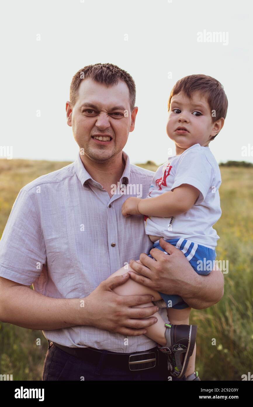 Papà tiene il suo figlio tra le braccia e lo abbraccia in un campo estivo al tramonto di sera. Amore di papà, attaccamento al bambino. Foto Stock