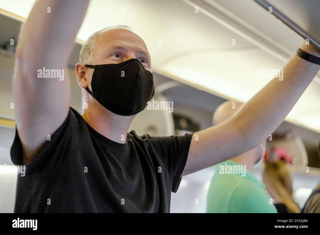 Uomo nella maschera di protezione mettendo la sua borsa in ripiano superiore in aereo Foto Stock